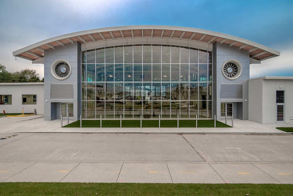 The front of the barrel-roofed Epps Aviation building displays a wall of windows and jet engines, an interesting focal point. 